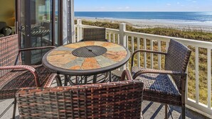 A balcony with wicker furniture and a glass door leading to a room. - Sea Cloisters II Ocean Front Beach Retreat (North Myrtle Beach)