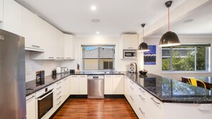 Cozinha moderna com armários brancos, eletrodomésticos de aço inoxidável, bancada de mármore preto e uma grande janela com vista para o exterior.