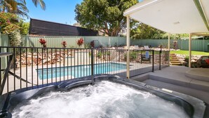 Um quintal com piscina, banheira de hidromassagem e área de varanda coberta.
