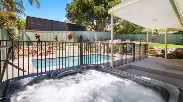 A backyard with a swimming pool, a hot tub, and a covered patio area.