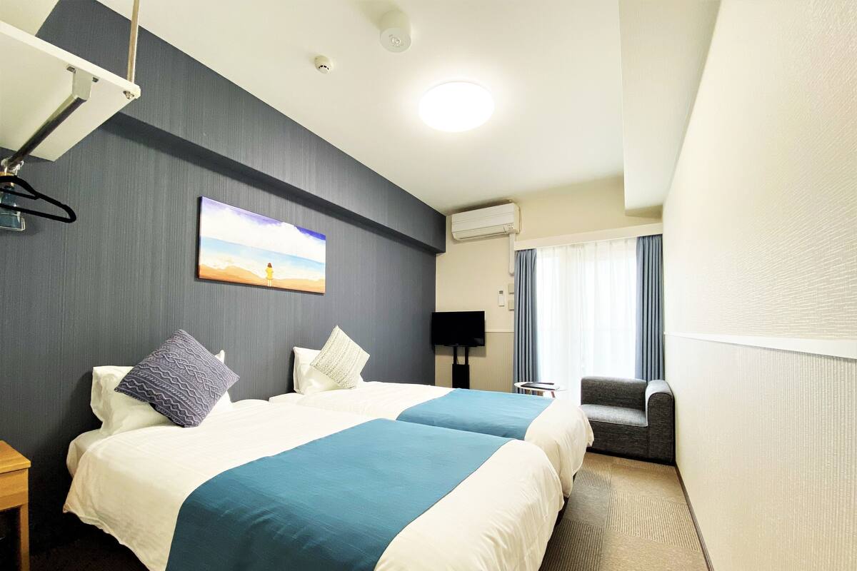 Ein Hotelzimmer mit zwei Betten, einem Fernseher, einem Sessel und einem Bild an der Wand.