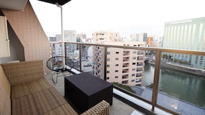 Een balkon met rieten meubels, een zwarte tafel en uitzicht op een rivier en stadsgebouwen.