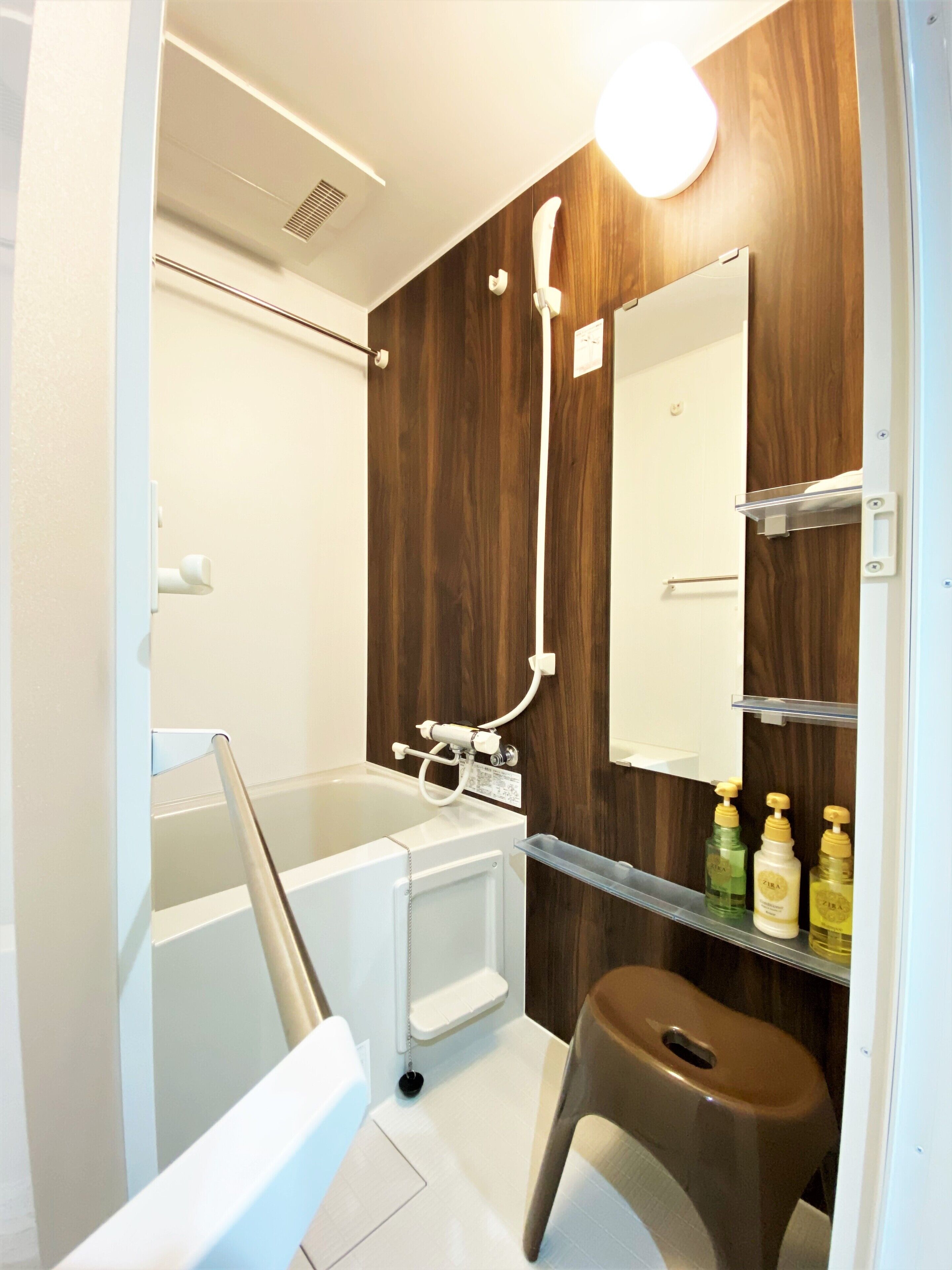 A modern bathroom with a wooden accent wall, a white bathtub, a shower, and a small stool.