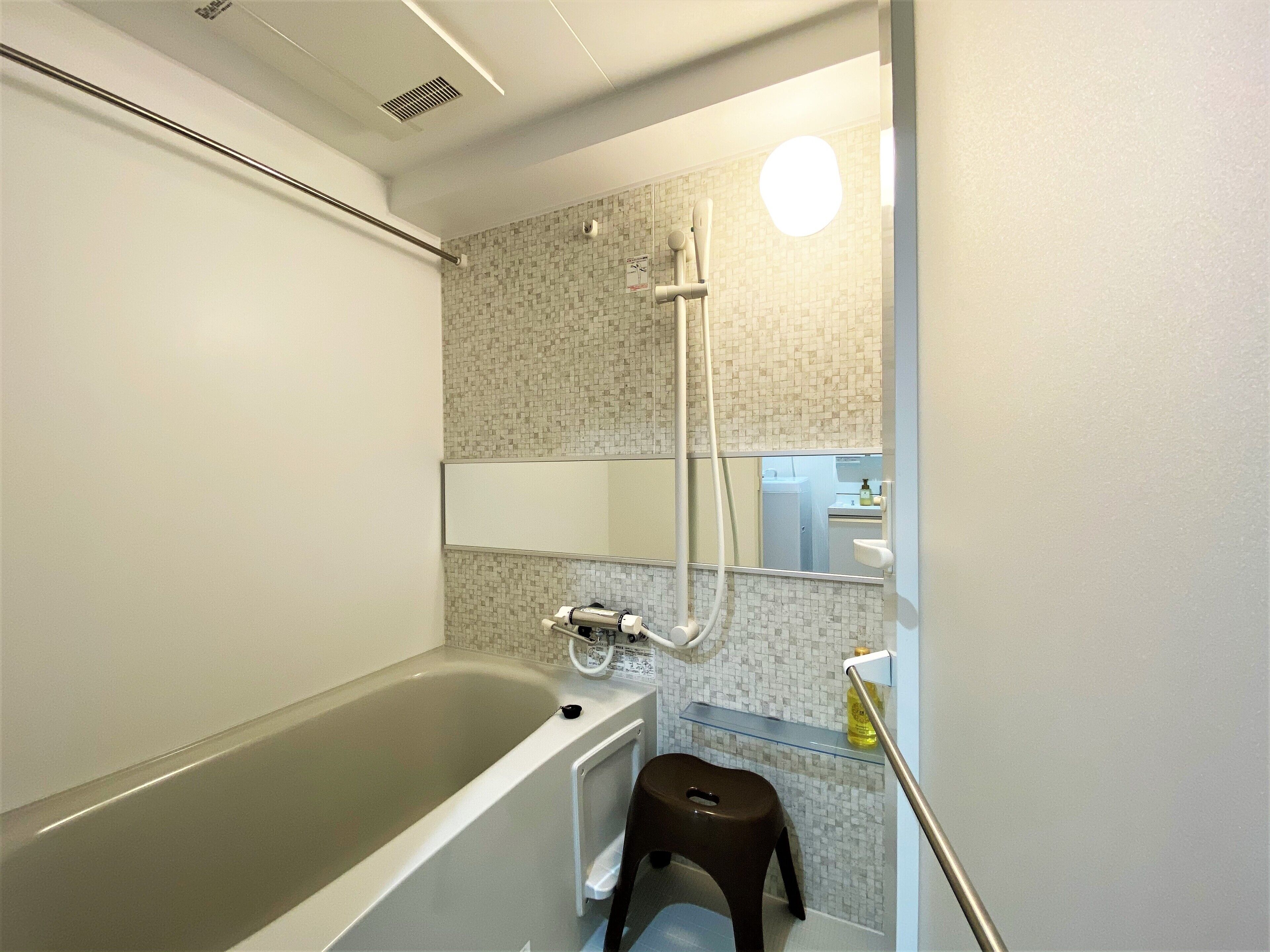 A modern bathroom with a bathtub, a shower, a toilet, and a small stool.