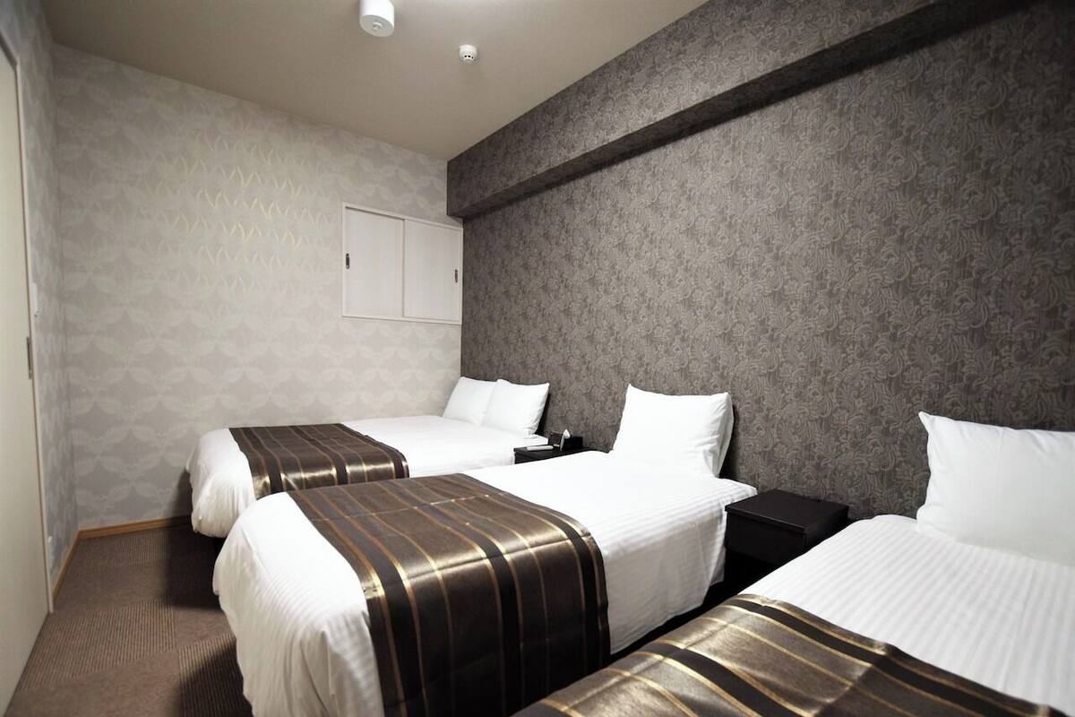 Ein Hotelzimmer mit drei Betten, einer grau gemusterten Wand und einer weißen Tür.