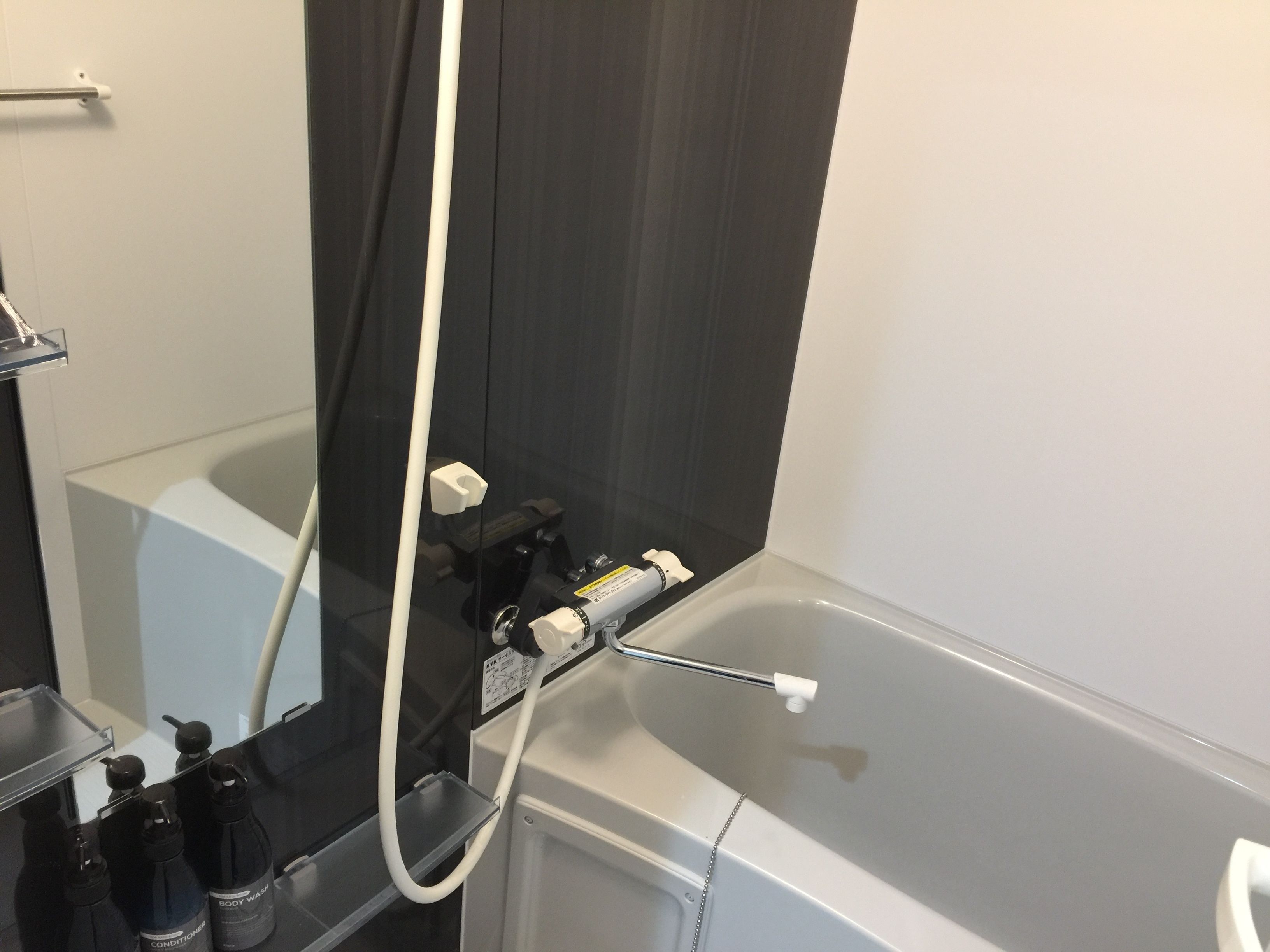A bathroom with a bathtub, a shower, and a mirror. There are bottles of body wash and conditioner on the sink.
