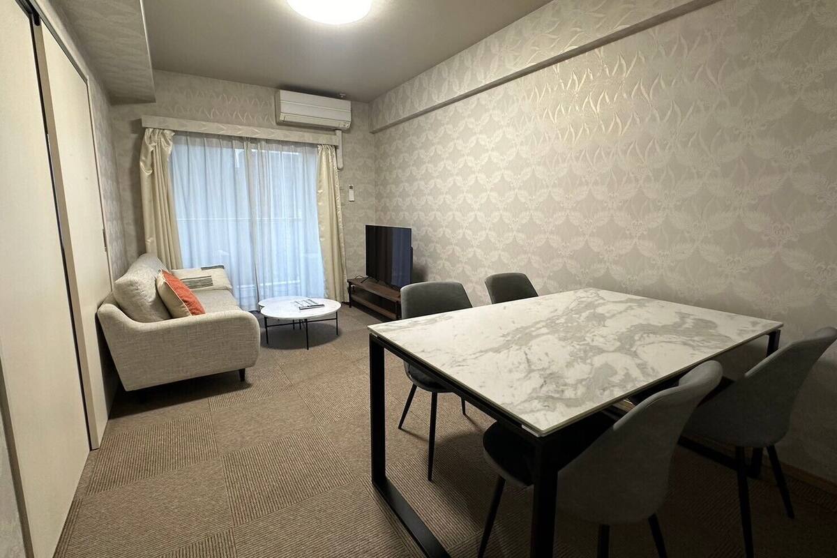 Ein Hotelzimmer mit Sofa, einem kleinen runden Tisch, einem Fernseher und einem Esstisch mit Stühlen.