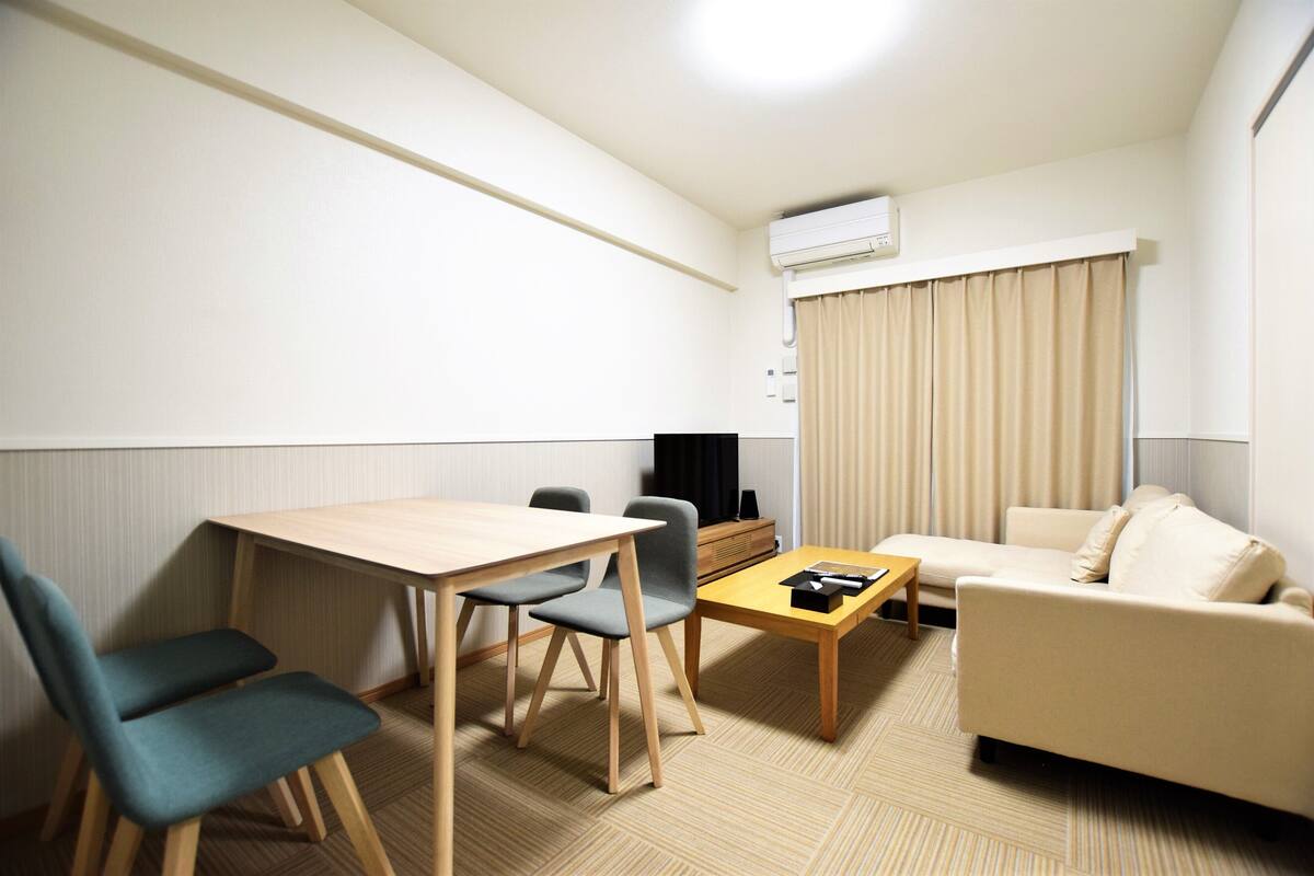 Ein modernes Hotelzimmer mit einem Holztisch, zwei Stühlen, einem Sofa, einem kleinen Couchtisch und einem Fernseher.