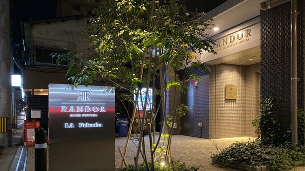 Een hotelentree met een bordje voor 'RANDOR HOTEL FUKUOKA' en een goed verlicht pad naar het gebouw.
