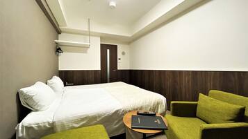Una habitación de hotel con una cama, un sillón verde, una mesita con un libro y una puerta.