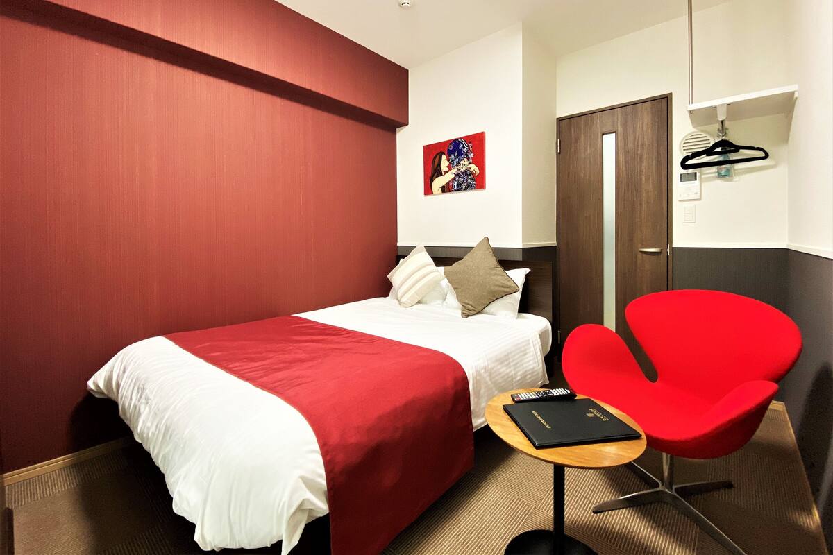 Ein Hotelzimmer mit einem Bett, einem roten Sessel, einem kleinen Tisch und einem Bild an der Wand.