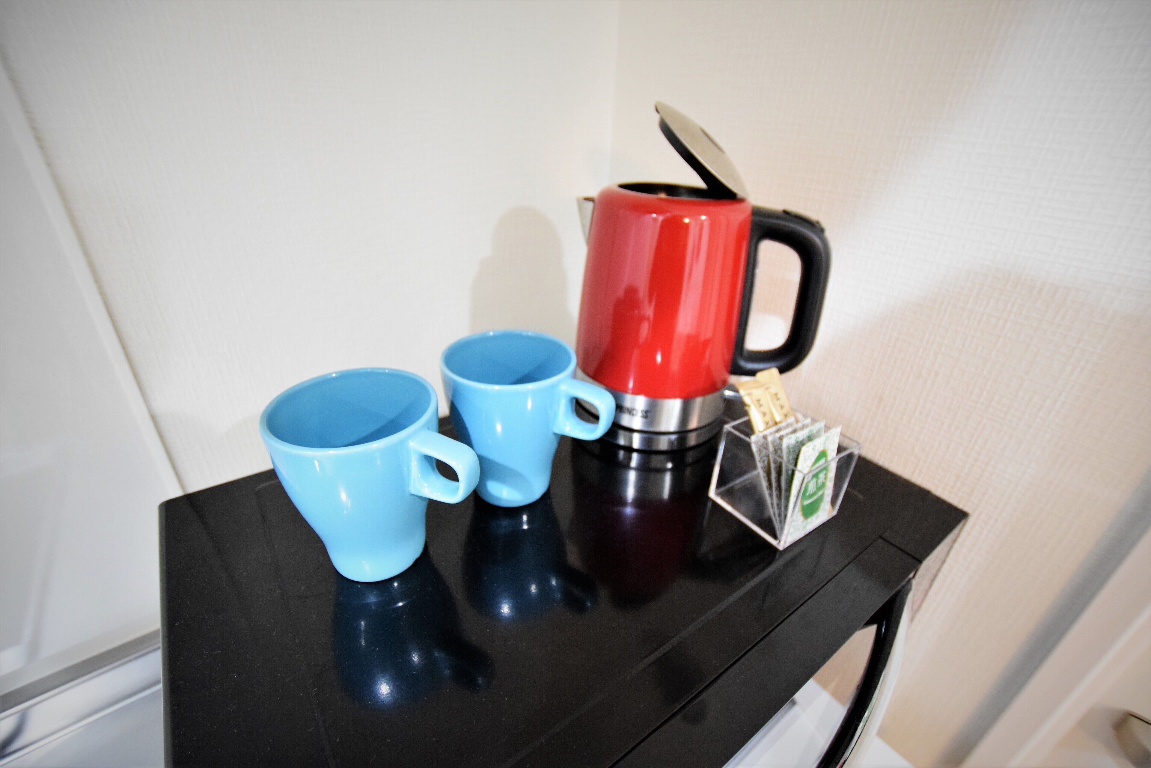 A black table with three blue cups and a red and black coffee maker.