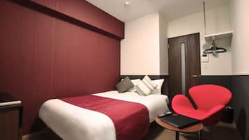 Een hotelkamer met twee bedden, een rode stoel, een klein tafeltje en een kledingkast.