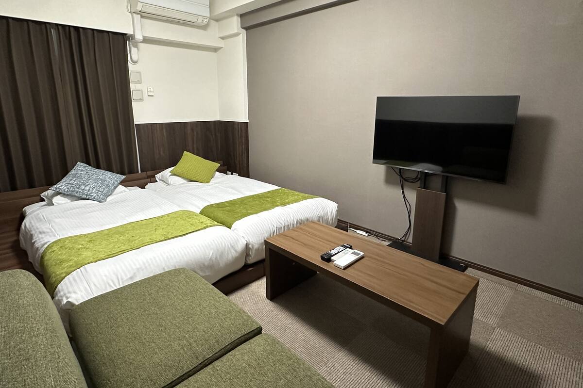 Ein Hotelzimmer mit zwei Betten, einem Fernseher, einem Schreibtisch und einem Sofa.