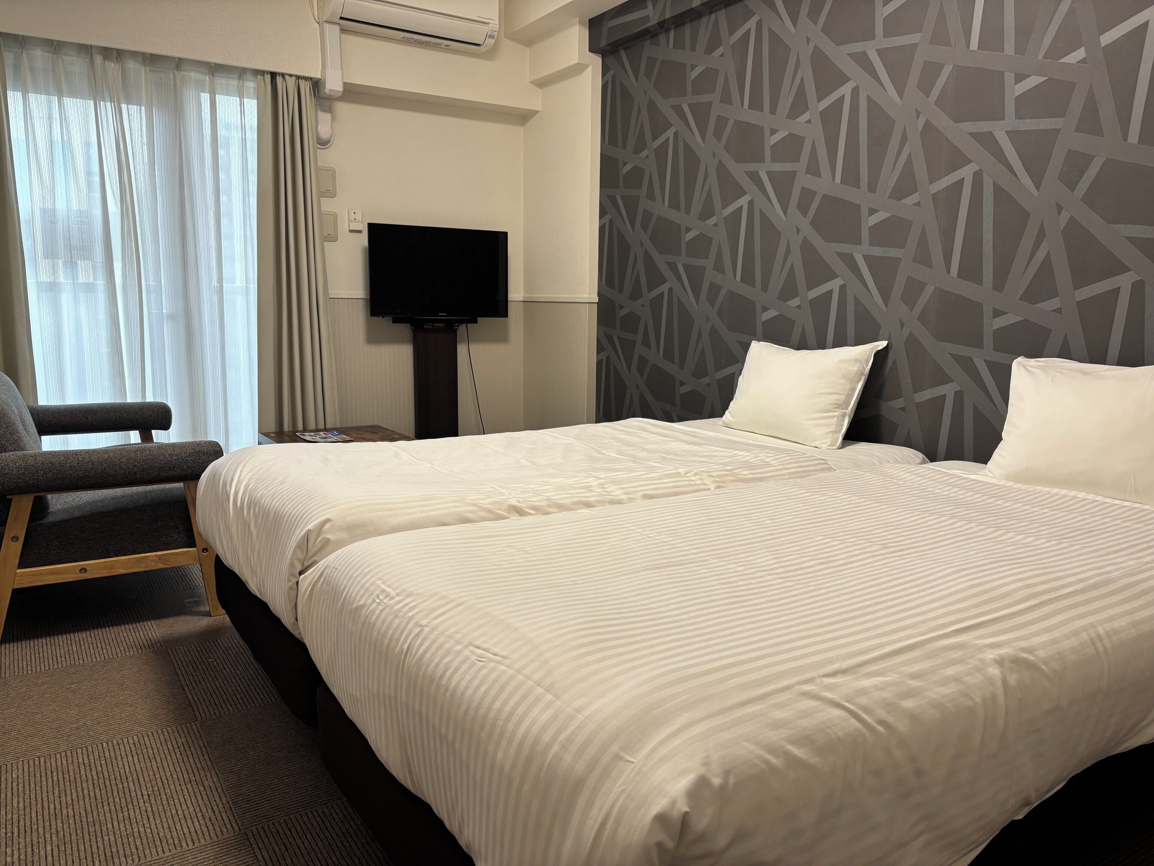 Een hotelkamer met een bed, een stoel, een televisie en een behang met patroon.