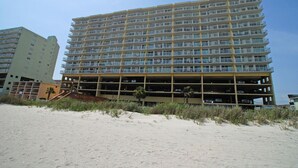 A multi-story hotel with a parking garage below the main structure, situated on a sandy beach with vegetation in the foreground. - Sunrise Pointe Oceanfront Resort (North Myrtle Beach)