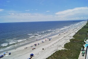 A beach with a long stretch of sand, a few umbrellas, and a few people. - Sunrise Pointe Oceanfront Resort (North Myrtle Beach)
