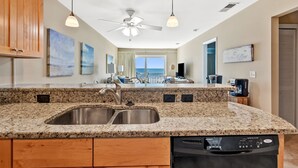 A kitchen with granite countertops, stainless steel sink, wooden cabinets, and a dishwasher. - Sea Cloisters II Ocean Front Beach Retreat (North Myrtle Beach)