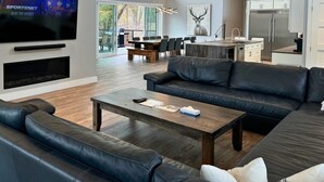 A modern living room with a large TV, leather sofas, a wooden coffee table, and a dining area with a large table and chairs. - Indoor Pool & Hot Tub, Steps to Ski Lift (Blue Mountains)