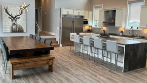 A modern kitchen with a central island, white bar stools, and a wooden dining table with benches. - Indoor Pool & Hot Tub, Steps to Ski Lift (Blue Mountains)