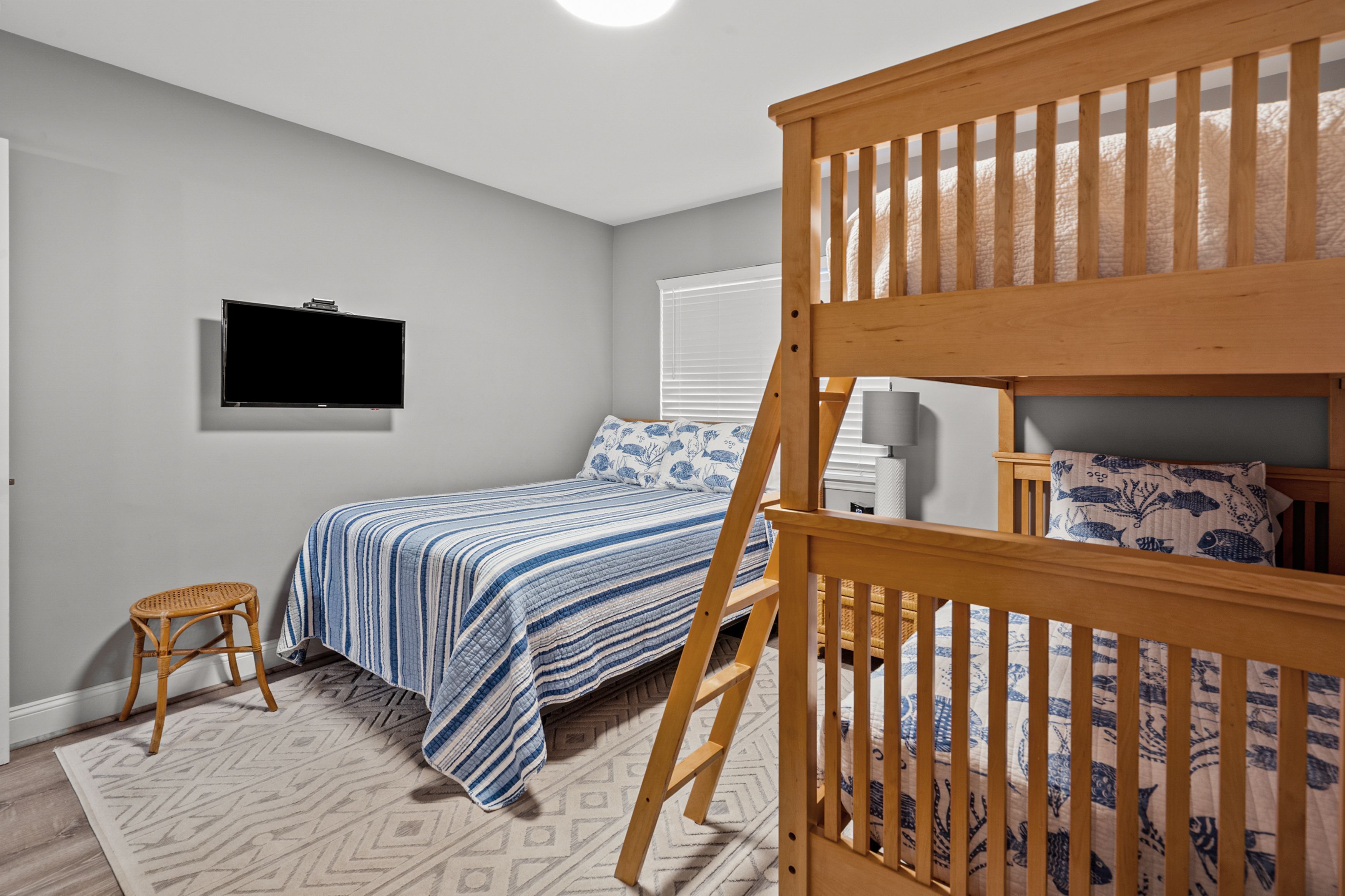 A bedroom with a bunk bed, a single bed, a television mounted on the wall, and a patterned rug.