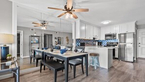 A modern kitchen with white cabinets, stainless steel appliances, and a dining area with a wooden table and chairs. - Sea Cloisters II Ocean Front Beach Retreat (North Myrtle Beach)