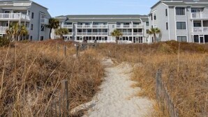 A beachfront hotel with multiple-story buildings, a sandy pathway leading to the entrance, and a clear blue sky. - Sea Cloisters I Ocean Front Beach Retreat (North Myrtle Beach)