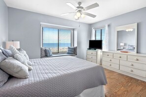 Une chambre à coucher comprenant un lit, un ventilateur de plafond, une commode, un téléviseur et une fenêtre avec des stores.