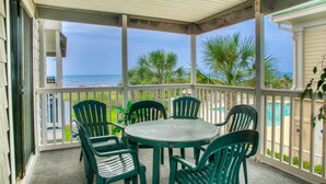 A covered outdoor area with a round table and chairs, a view of the ocean, and a pool in the background. - Sea Cloisters II Ocean Front Beach Retreat (North Myrtle Beach)