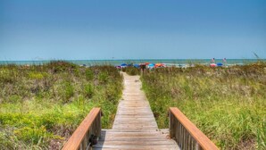 A wooden boardwalk leading to a beach with colorful umbrellas and flags. - Sea Cloisters II Ocean Front Beach Retreat (North Myrtle Beach)