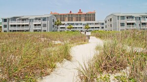 A beachfront hotel with multiple-story buildings, a sandy pathway, and surrounding beach vegetation. - Sea Cloisters II Ocean Front Beach Retreat (North Myrtle Beach)