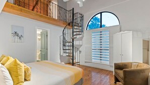 A bedroom with a bed, a chair, a wardrobe, a spiral staircase, and a large window. - The Self-Sustainable Beach House (South Padre Island)