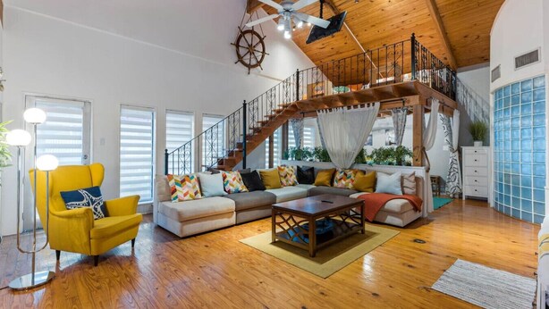 A spacious living room with a wooden ceiling, a staircase, and a large window. - The Self-Sustainable Beach House (South Padre Island)