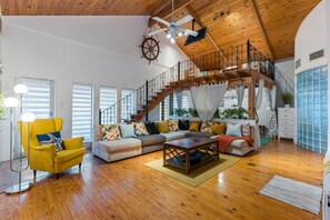 A spacious living room with a wooden ceiling, a staircase, and a large window. - The Self-Sustainable Beach House (South Padre Island)