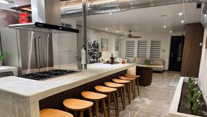A modern kitchen with a bar area, stainless steel appliances, and wooden stools. - The Self-Sustainable Beach House (South Padre Island)