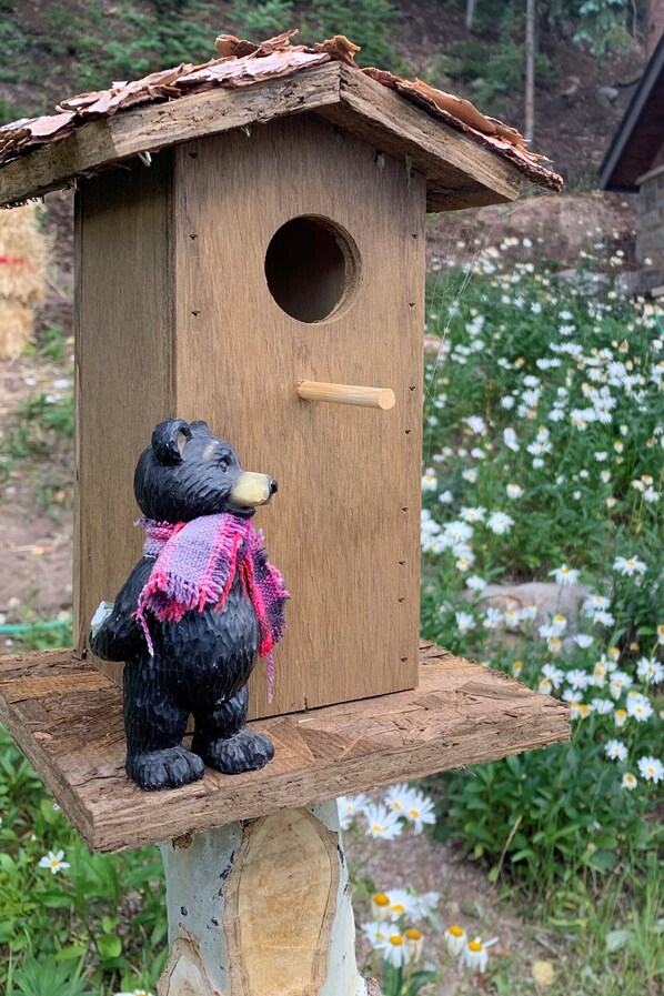 A wooden birdhouse with a bear figurine on top.