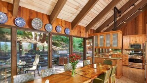 Eine geräumige Küche mit Holdekor-Schränken und einer großen Kochinsel, ein Essbereich mit Holztisch und Stühlen sowie ein Blick auf einen Garten durch große Fenster.