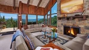 A spacious living room with a stone fireplace, large windows offering a mountain view, and a cozy seating area. - Beautiful 6BR house on Snowmass mountain w easy access to ski in and out (Snowmass Village)