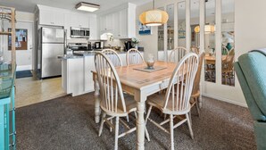 A modern kitchen with white cabinetry, stainless steel appliances, and a dining area with a wooden table and chairs. - Sea Cloisters I Ocean Front Beach Retreat (North Myrtle Beach)