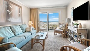 A hotel room with a balcony, a sofa, a chair, a table, and a TV. - Sea Cloisters I Ocean Front Beach Retreat (North Myrtle Beach)