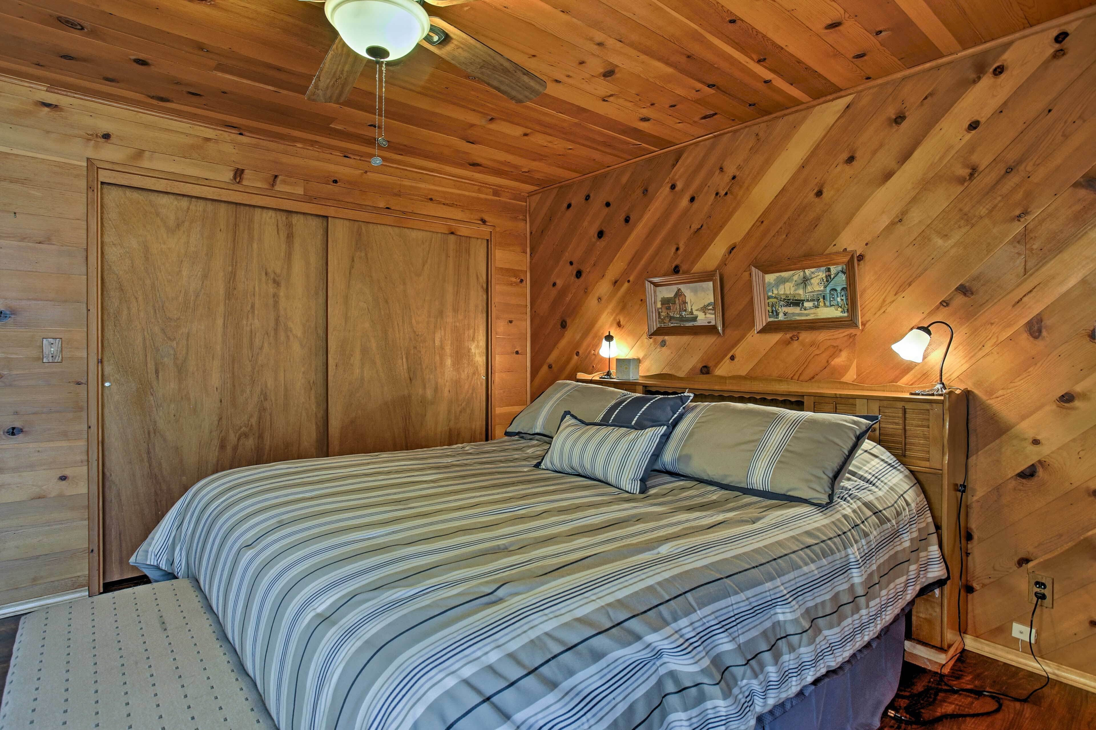 Un dormitorio con paneles de madera, una cama, dos lámparas de noche y un ventilador de techo.