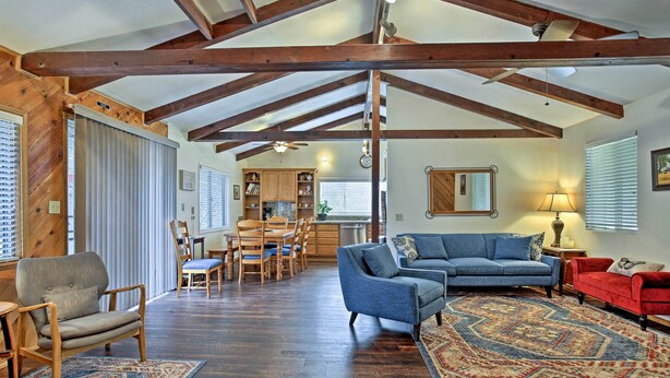 A spacious living area with a high ceiling, wooden beams, a blue sofa, a red armchair, and a dining set. - Cozy Home w/ Patio Near Yosemite National Park! (Mariposa)