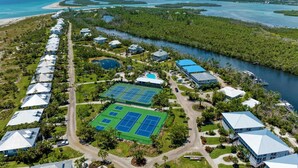 An aerial view of a resort with multiple buildings, a tennis court, and a water body.