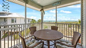 A covered outdoor area with a table and chairs, a ceiling fan, and a view of the beach.