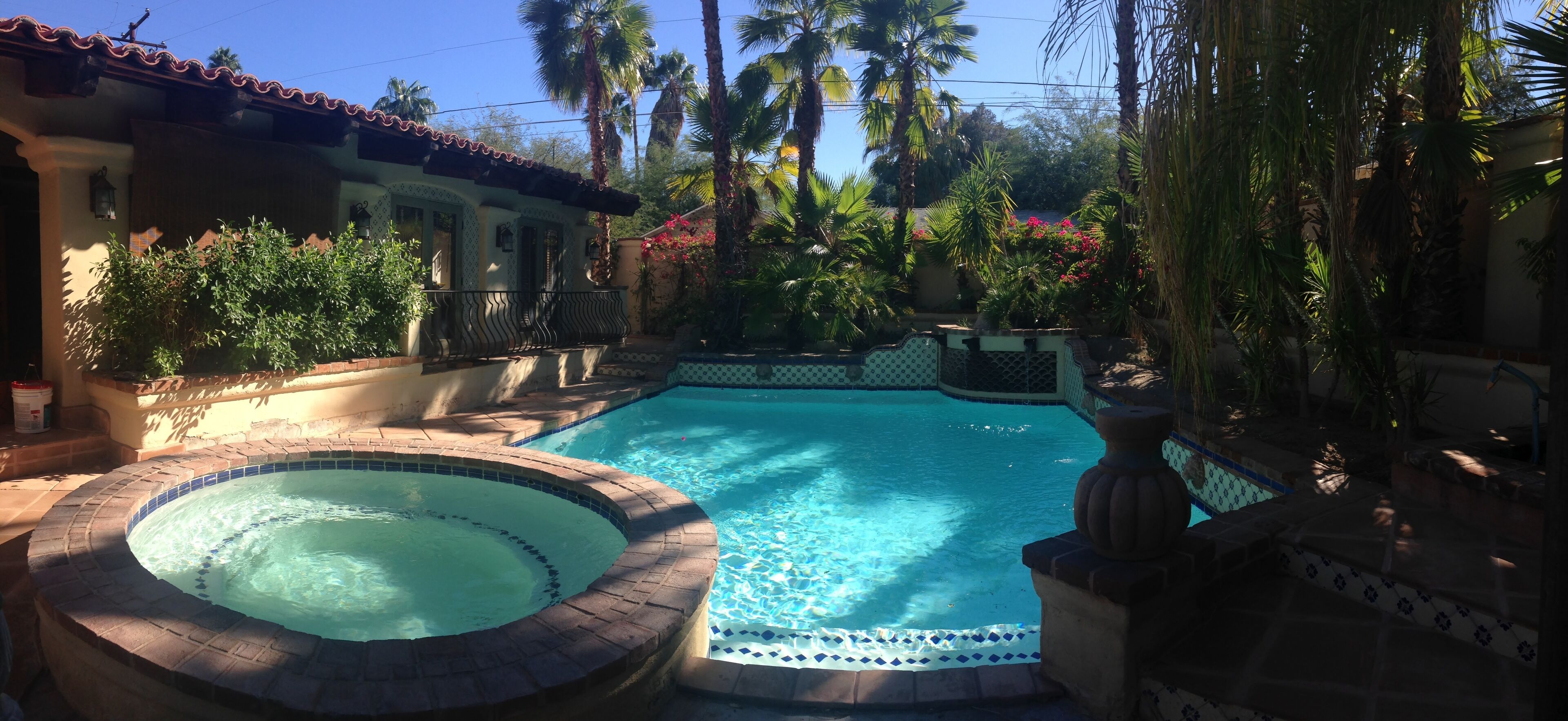 A swimming pool with a hot tub, surrounded by palm trees and a tiled deck.
