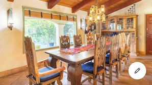 Un comedor con mesa y sillas de madera, una araña y vistas al exterior a través de una ventana.