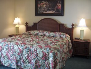 Una cama bien hecha con un edredón floral, dos lámparas de noche, un cuadro en la pared y un cabecero de madera.