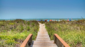 A wooden boardwalk leading to a beach with colorful umbrellas and flags. - Sea Cloisters II Ocean Front Beach Retreat (North Myrtle Beach)