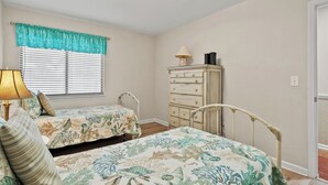A bedroom with two beds, a dresser, a lamp, and a window with blinds. - Sea Cloisters II Ocean Front Beach Retreat (North Myrtle Beach)