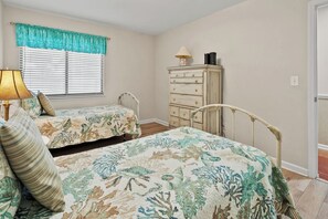 A bedroom with two beds, a dresser, a lamp, and a window with blinds. - Sea Cloisters II Ocean Front Beach Retreat (North Myrtle Beach)